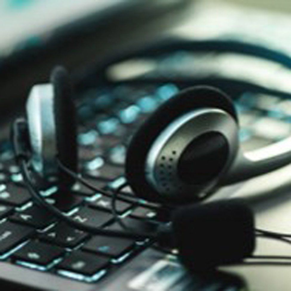 Headphones resting on a laptop keyboard. Black and silver with a coiled cord.