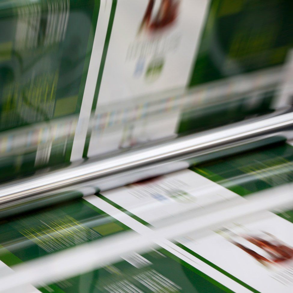 Printing press with a roll of green and white printed paper in motion.