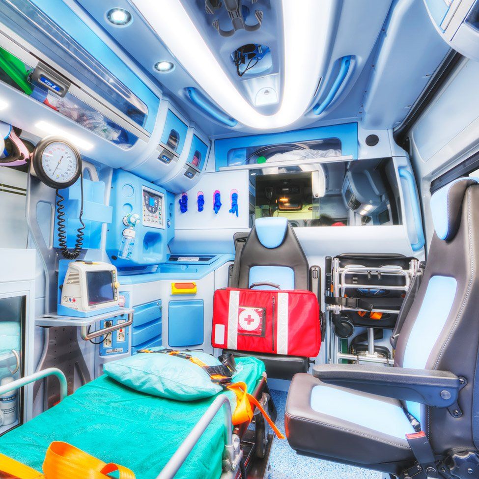 Interior of a modern ambulance. Medical equipment, patient stretcher, red medical kit, and two seats are visible.