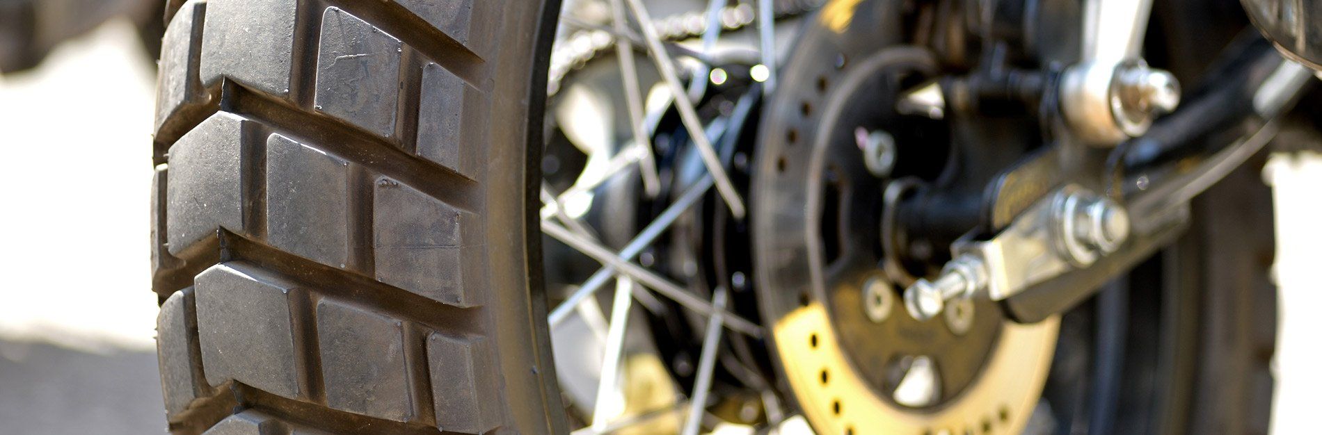 Close-up of a motorcycle rear wheel. The tire has a deep tread pattern. The disc brake and spokes are also visible.