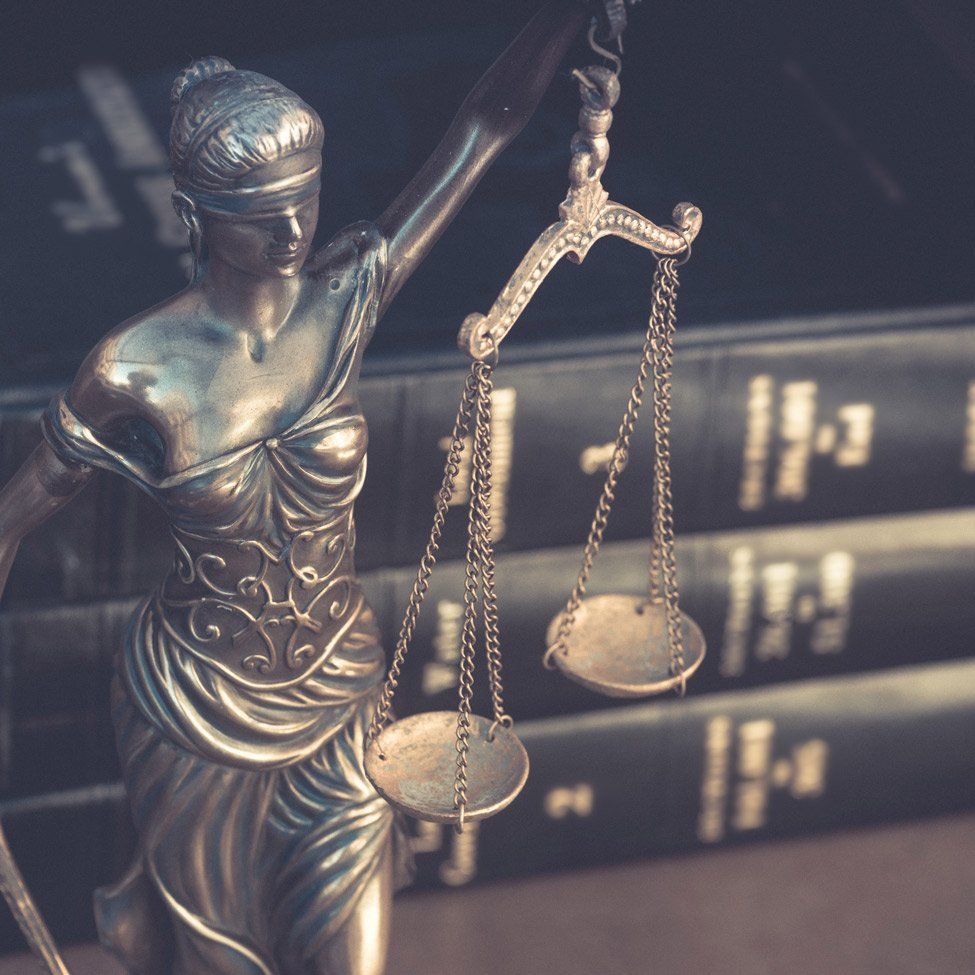 Statue of Lady Justice holding scales, in front of a stack of law books.