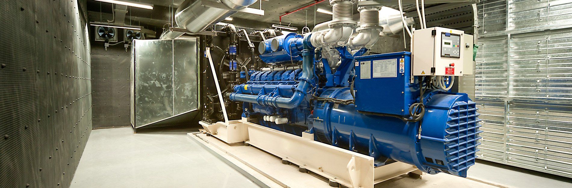 A large blue generator in a utility room. The machine is surrounded by metal panels and pipes.