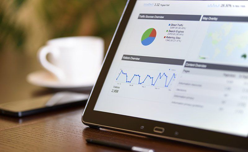 Tablet displaying data charts and graphs, with a coffee cup and phone on a table.