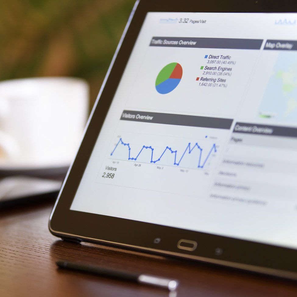 Tablet displaying data analytics: charts, graphs, pie chart. A pen and coffee cup sit nearby.