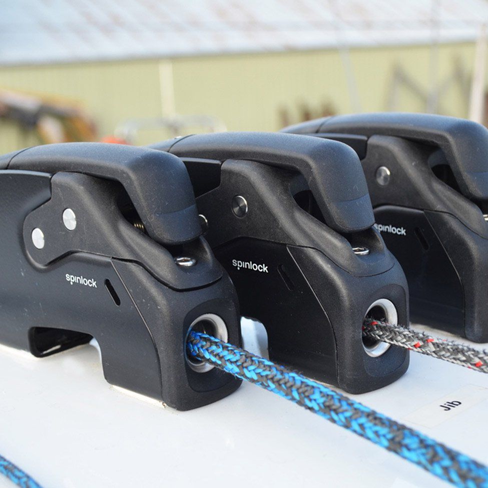 Three black Spinlock rope clutches on a white surface, holding colorful ropes.