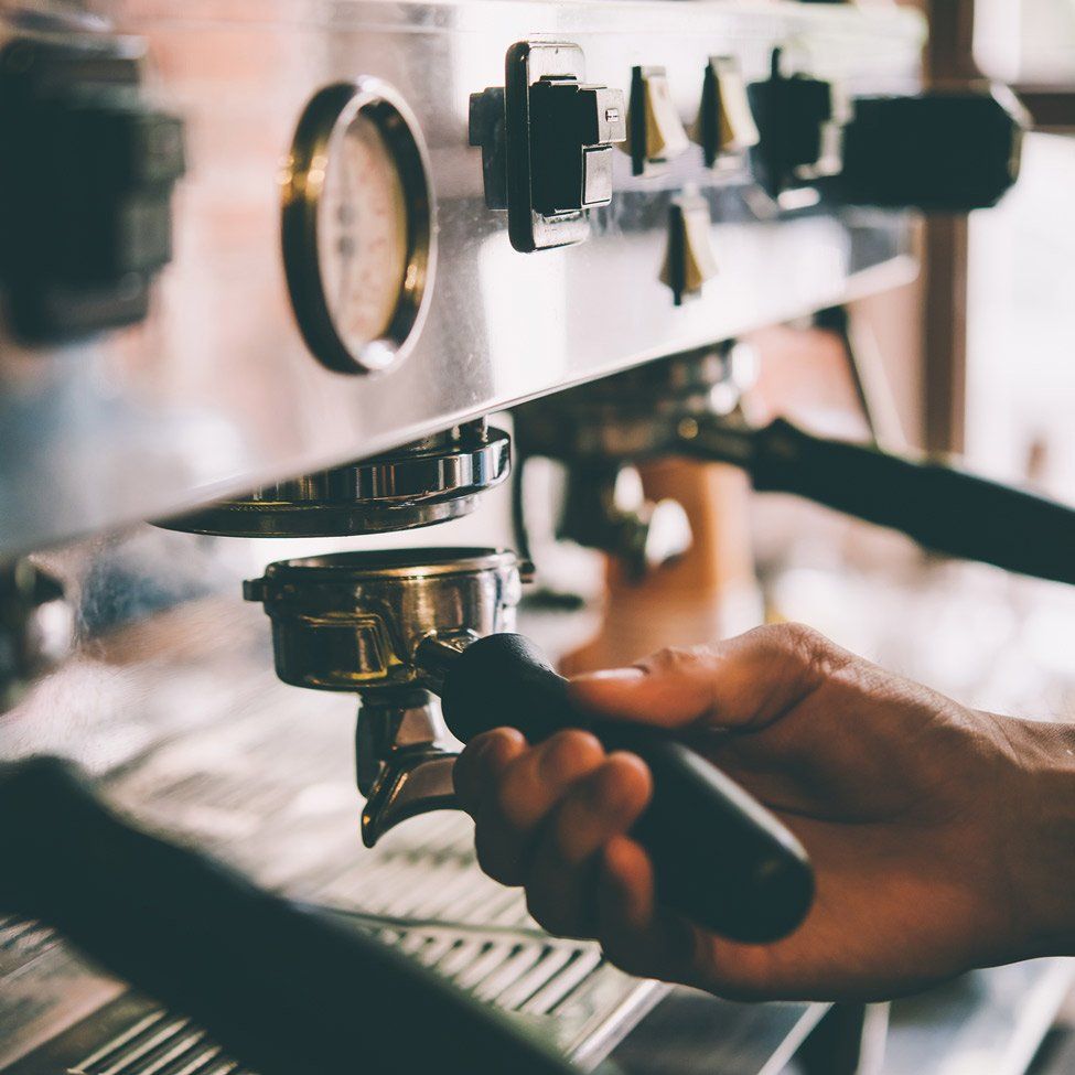 Hand holding a portafilter, preparing espresso with a commercial coffee machine.