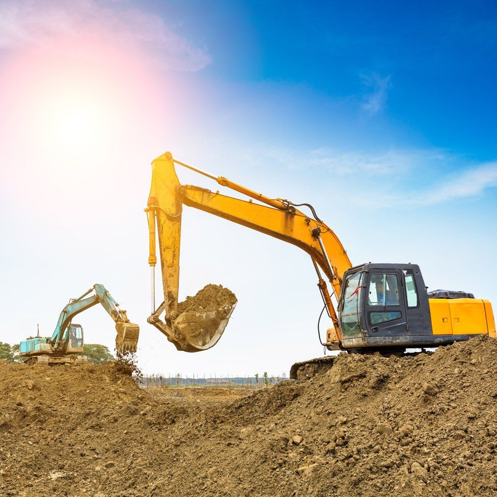 Two excavators digging earth on a construction site under a bright blue sky.