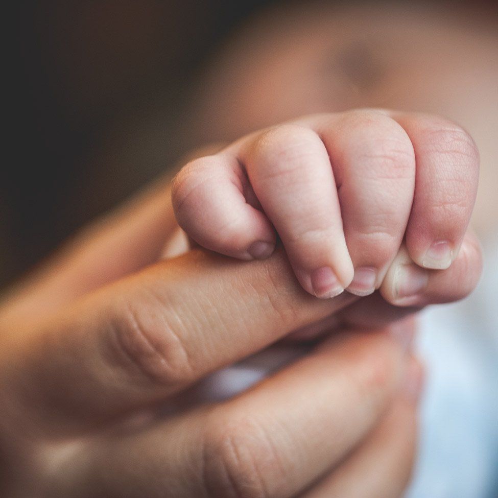 Baby's hand gripping an adult's finger. The baby's skin is soft and pink, and the adult's skin is tan.