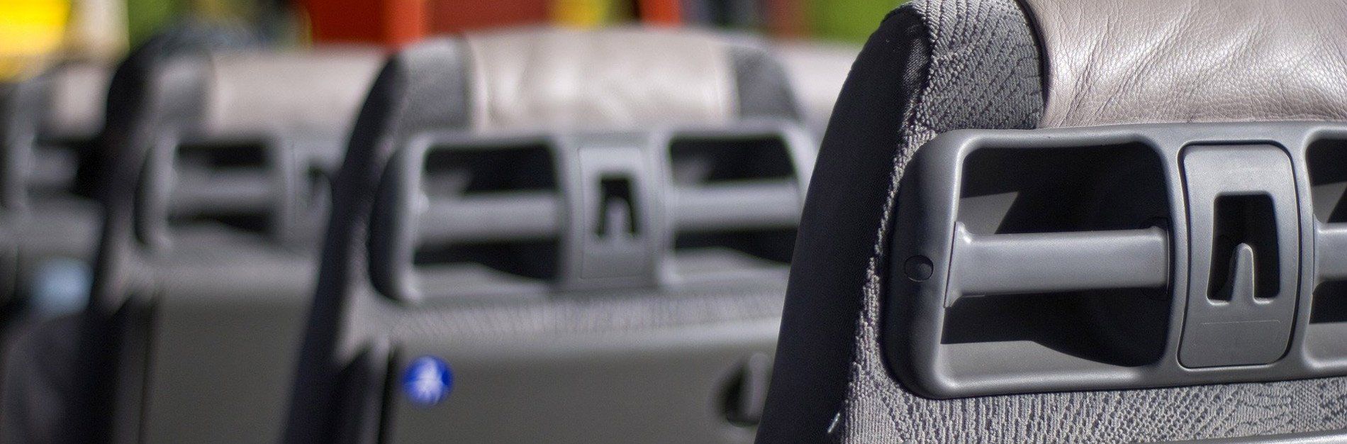 Rows of gray bus seats, with focus on the seatback detail of a vent or handle.