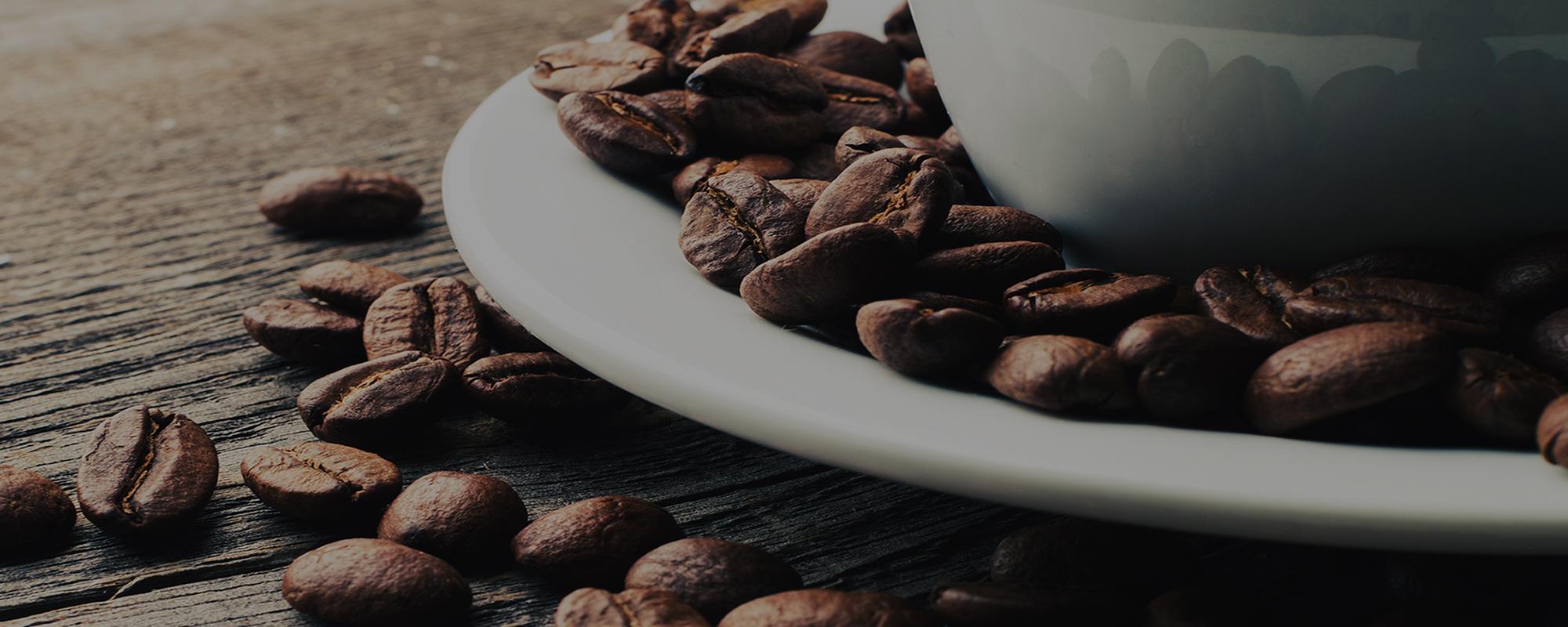 Coffee beans on a saucer, next to a white cup on a wooden surface.