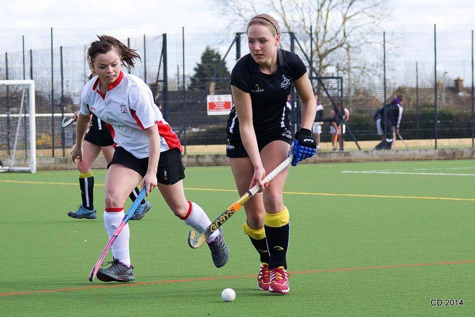 Two women are playing field hockey on a field.
