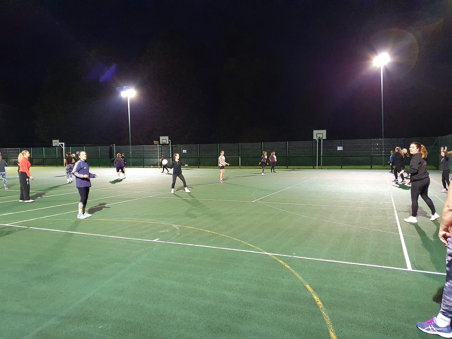 A group of people are playing a game of netball on a court at night.