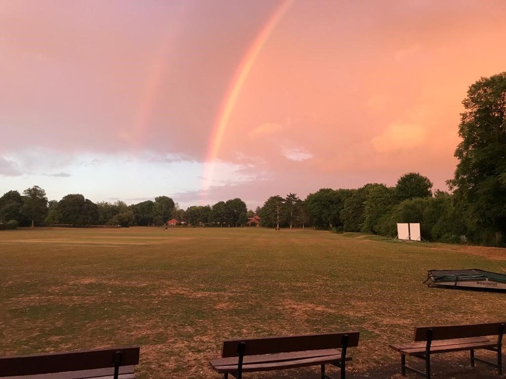 A rainbow is visible over a field with benches in the foreground.