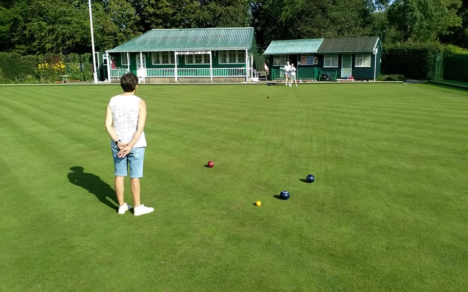 A woman is standing on a lush green field looking at bowling balls.