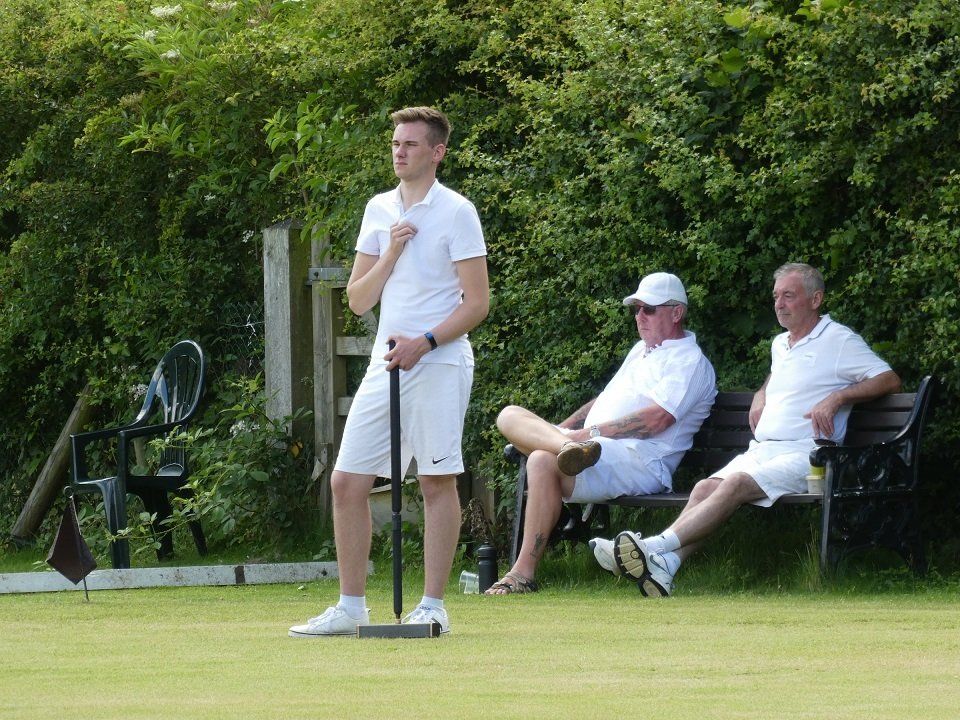 A man in a white shirt is standing next to two men sitting on benches.