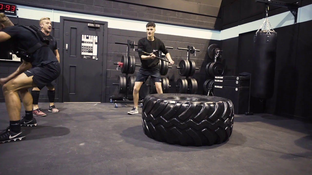 A group of people are jumping over a tire in a gym.
