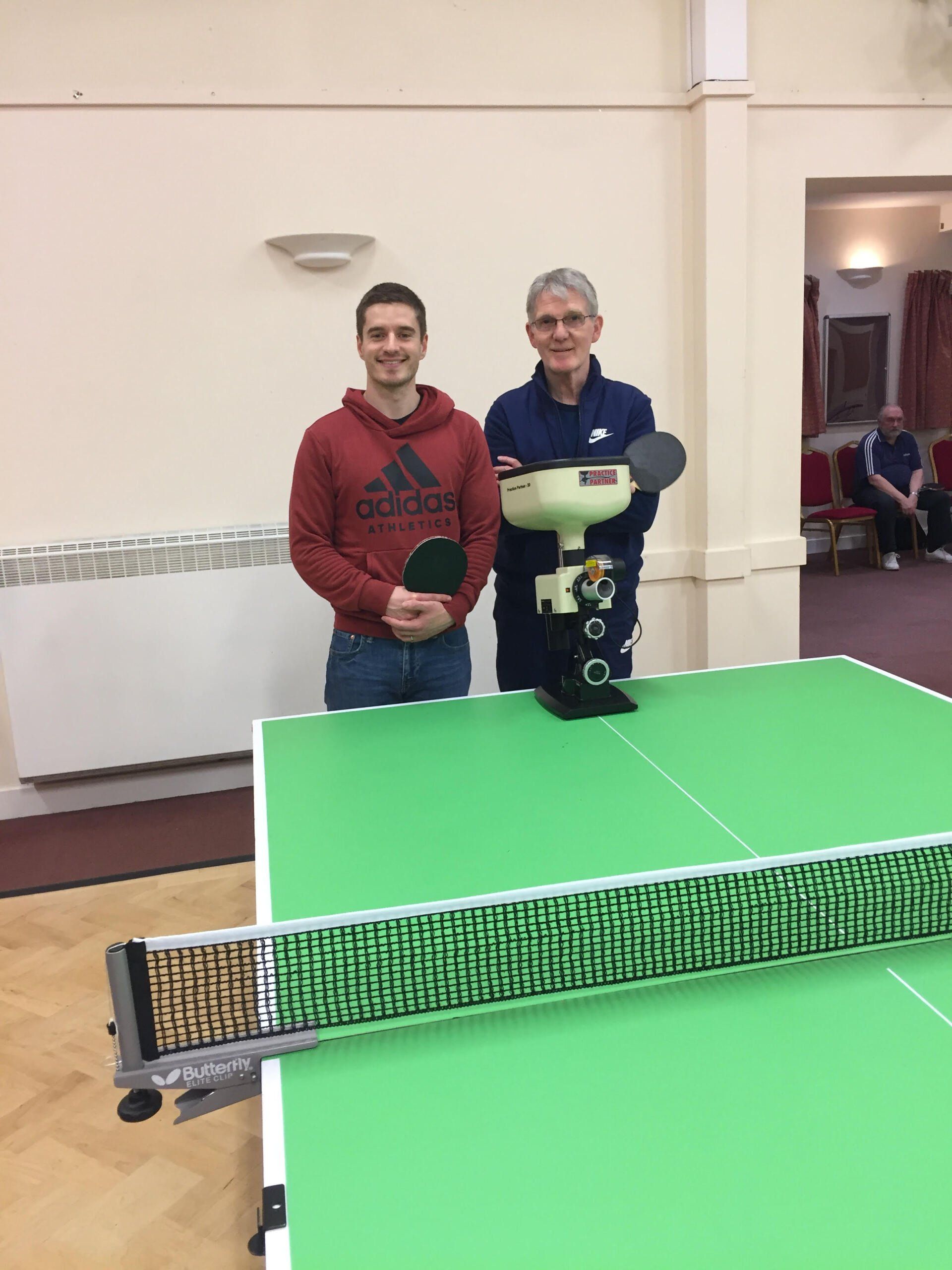 Two men are standing next to a ping pong table holding rackets.