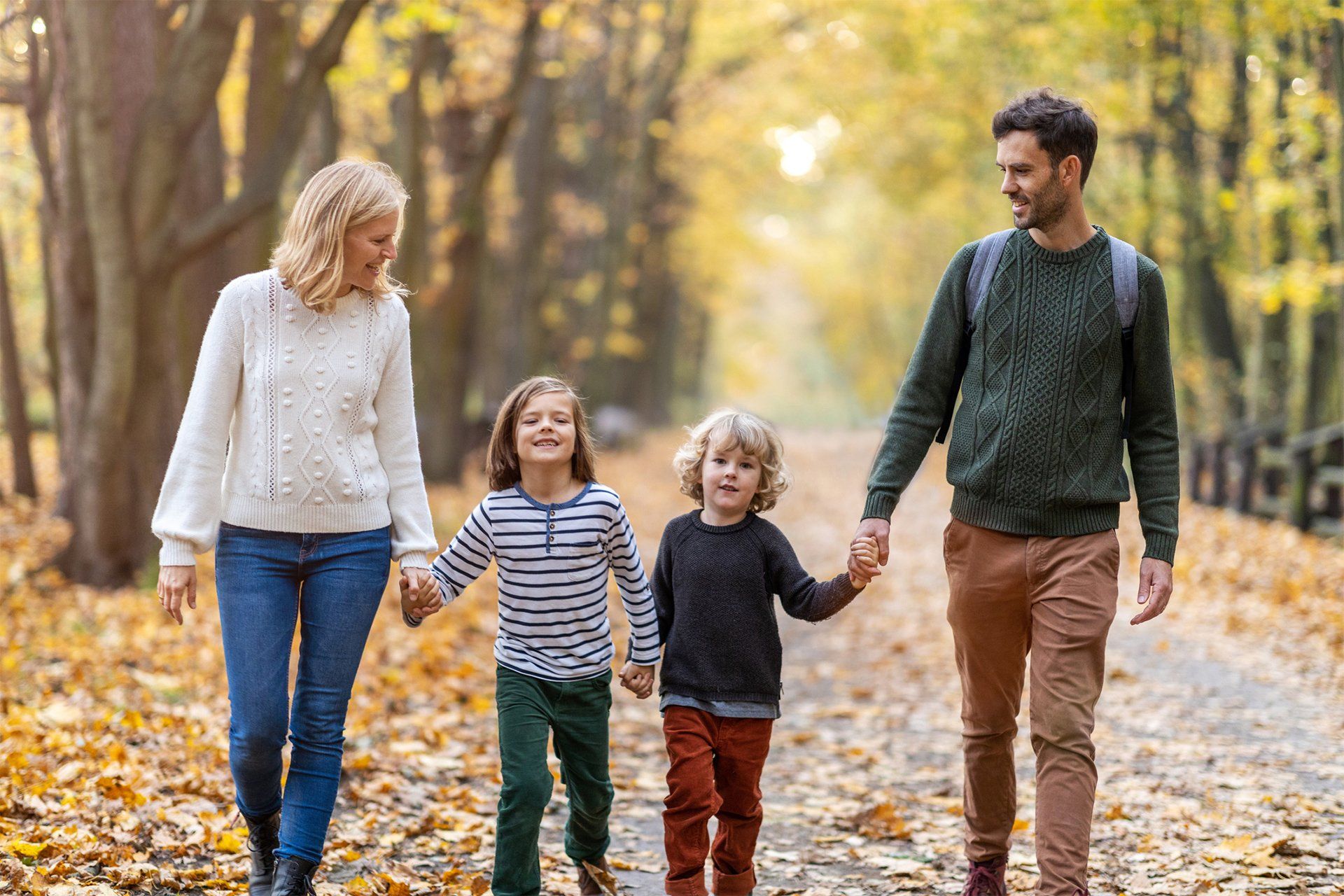 A young family walking outdoors with trees on both sides, enjoying nature together