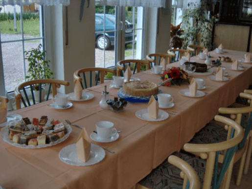 Langer Esstisch mit Geschirr, Kuchen und Gebäck. Stühle umgeben den Tisch in einem hellen Esszimmer.