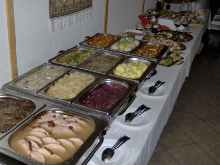 Buffettisch mit verschiedenen Gerichten, darunter Fleisch, Kartoffeln und Gemüse. Teller und Besteck sind bereitgestellt.