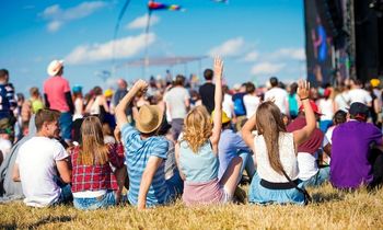 Menschen bei einem Musikfestival im Freien, die auf dem Rasen sitzen und sich eine Aufführung ansehen.