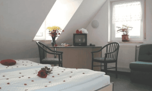 Schlafzimmer mit zwei mit Rosenblättern dekorierten Einzelbetten, Schreibtisch mit Fernseher und Fenster.