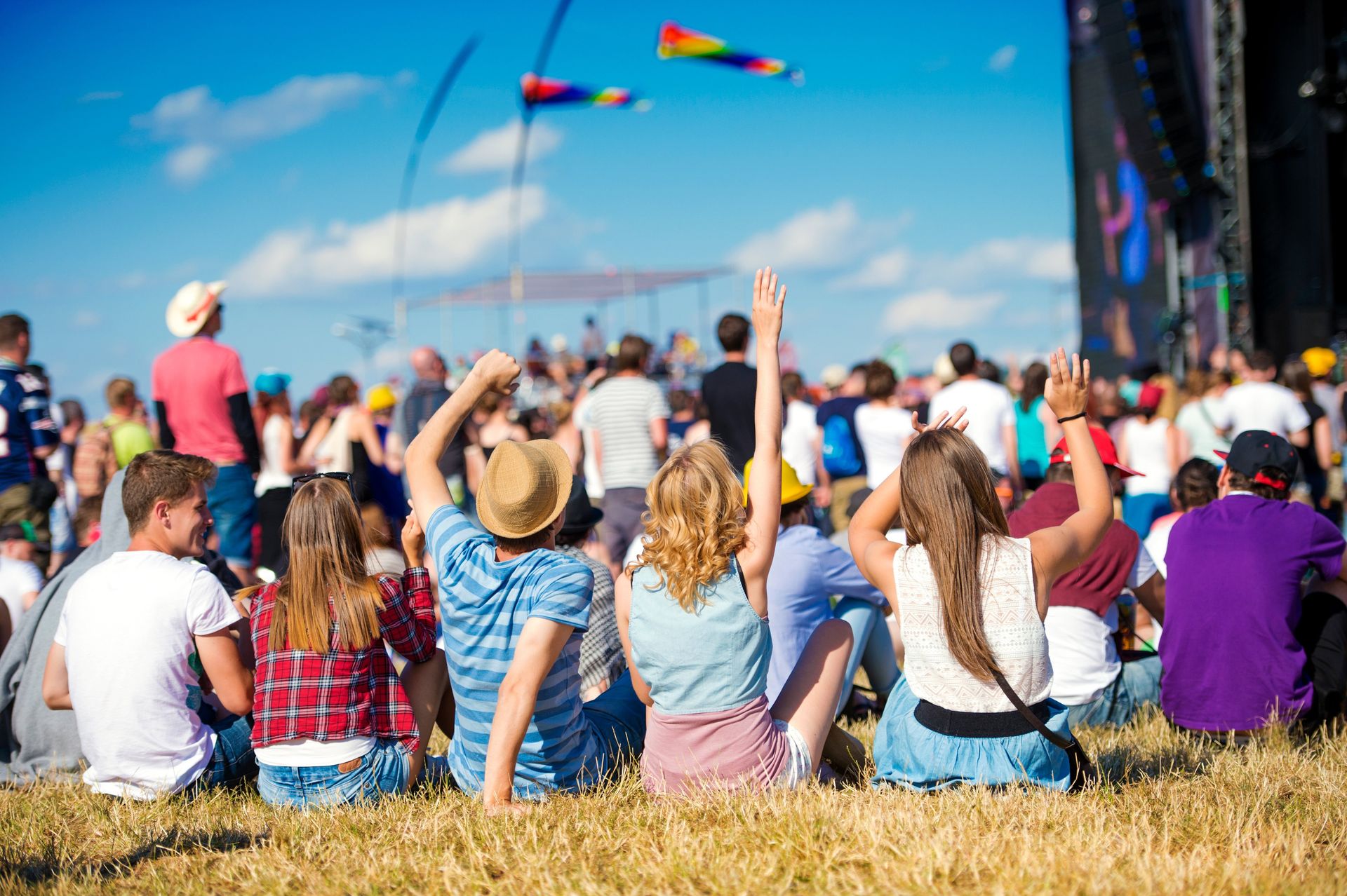 Menschen bei einem Musikfestival im Freien, die Arme unter blauem Himmel mit Drachen zur Bühne erhoben.