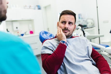 man in examination room holding right cheek in pain