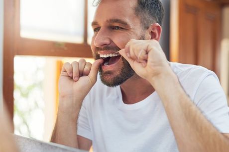 man flossing his teeth in front of window