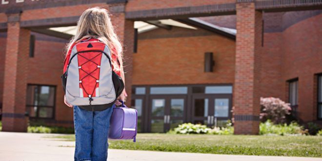 Young girl with lunchbox waiting outside school