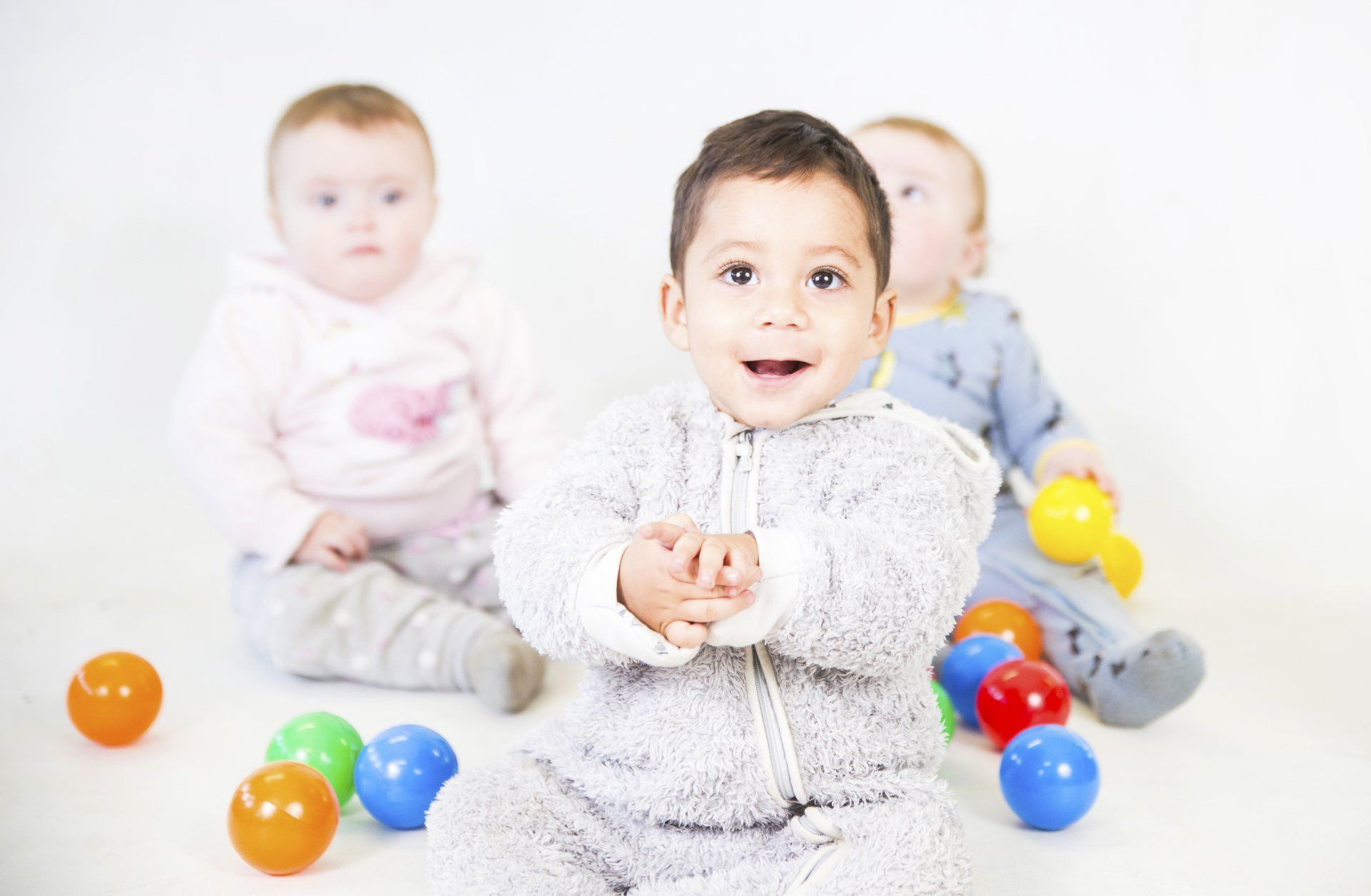 Three babies are sitting on the floor playing with balls.