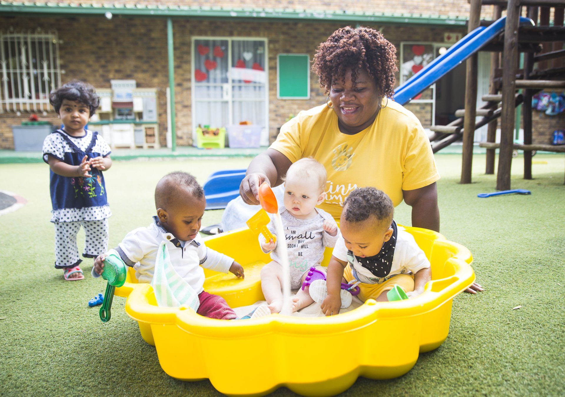 A woman is playing with three babies in a sandbox.