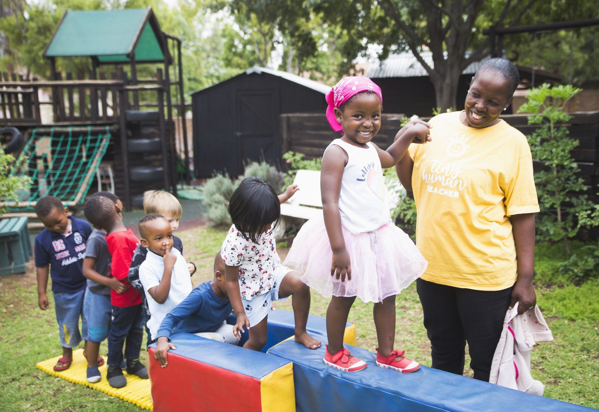 A woman is standing next to a group of children on a balance beam.