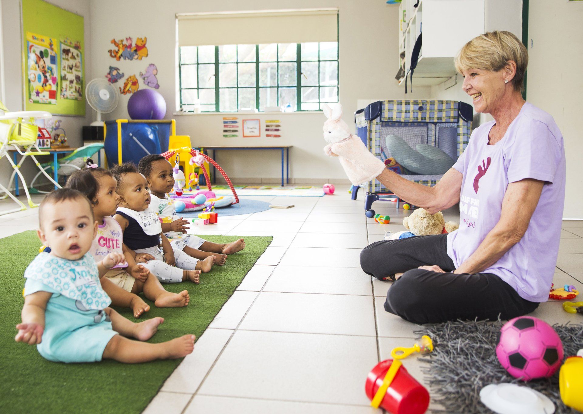 A woman is sitting on the floor reading a book to a group of babies.