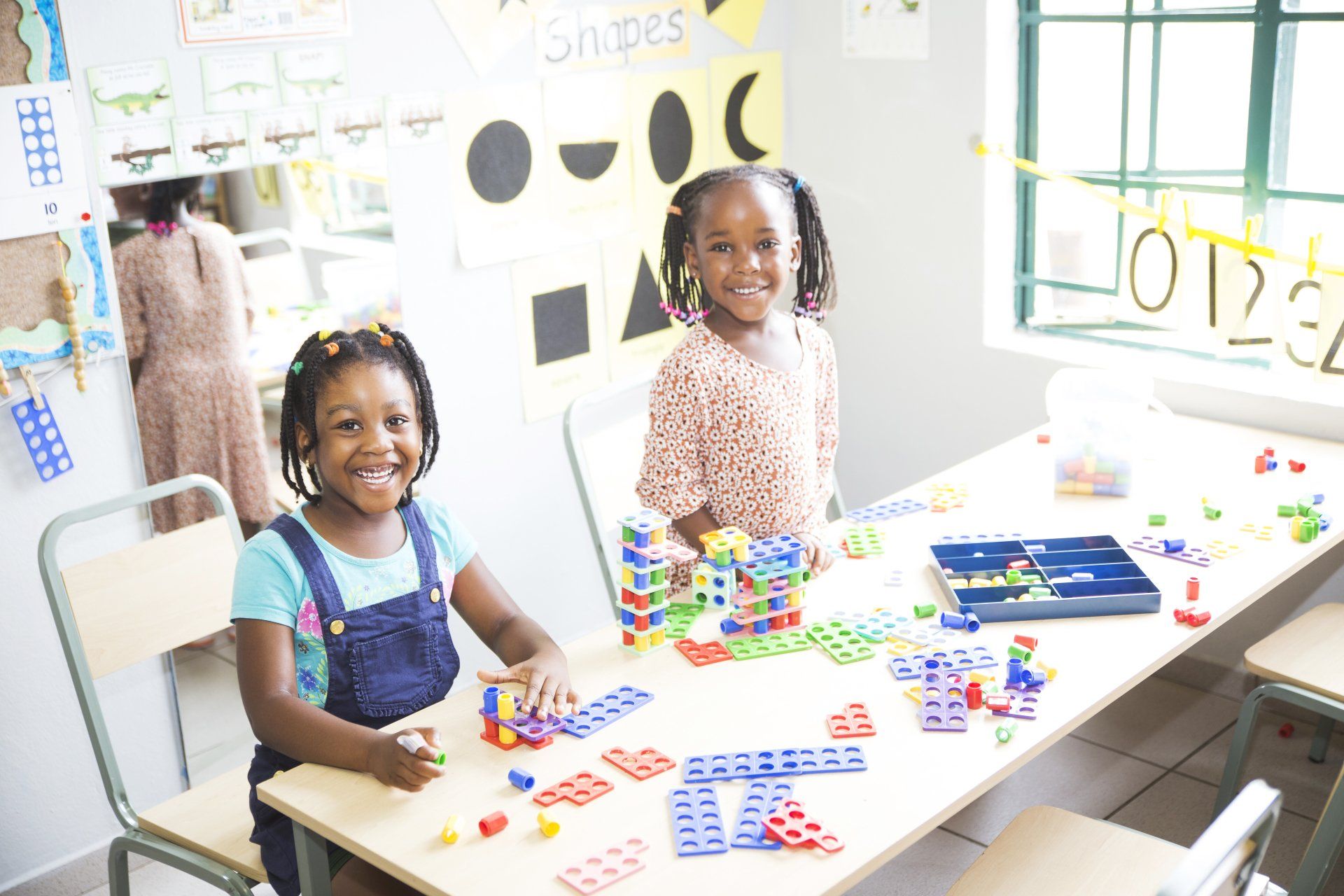 Two little girls are sitting at a table playing with lego blocks.