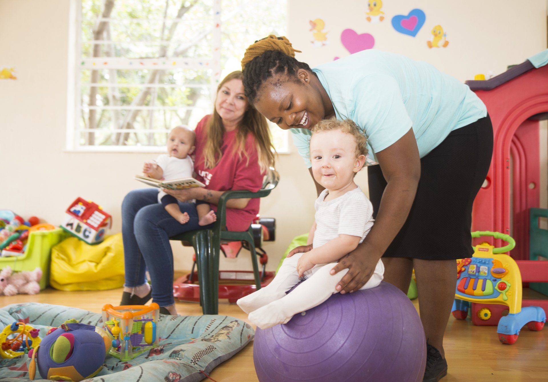 A woman is helping a baby sit on a purple exercise ball.