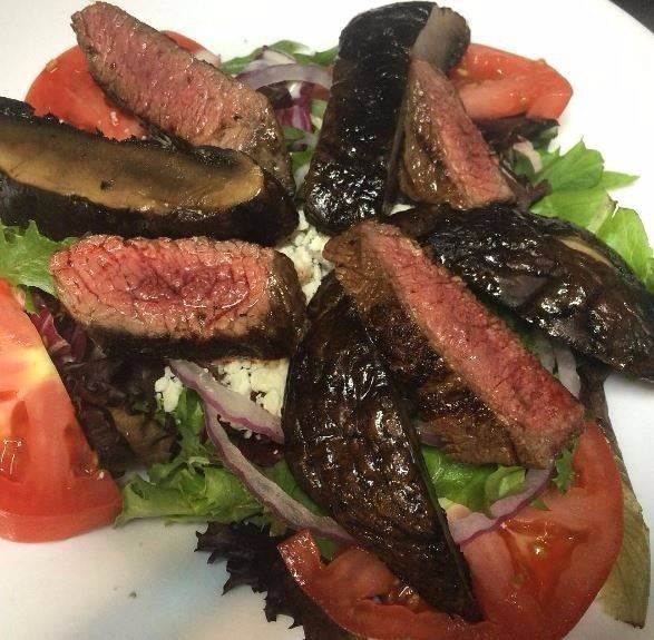 sliced steak and portobello mushrooms over a salad