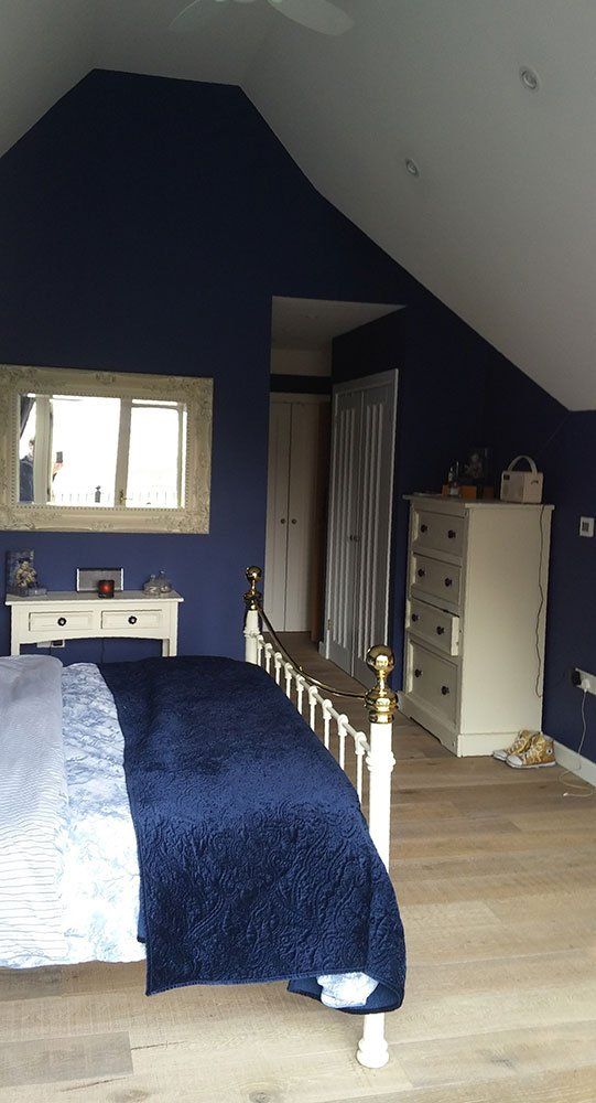 A bedroom with a bed , dresser , mirror and blue walls.