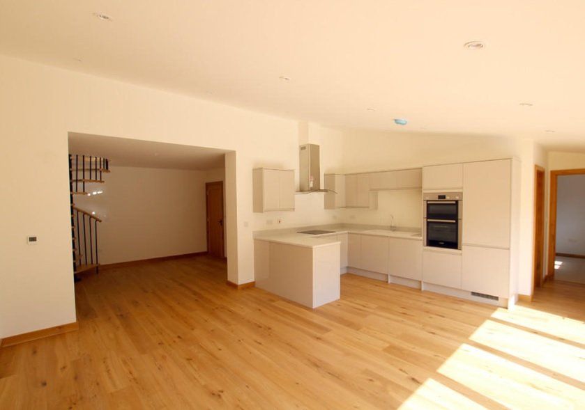 An empty kitchen with wooden floors and white cabinets