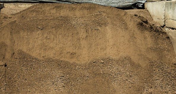 Pile of tan sand or soil heaped against a rough concrete wall outdoors