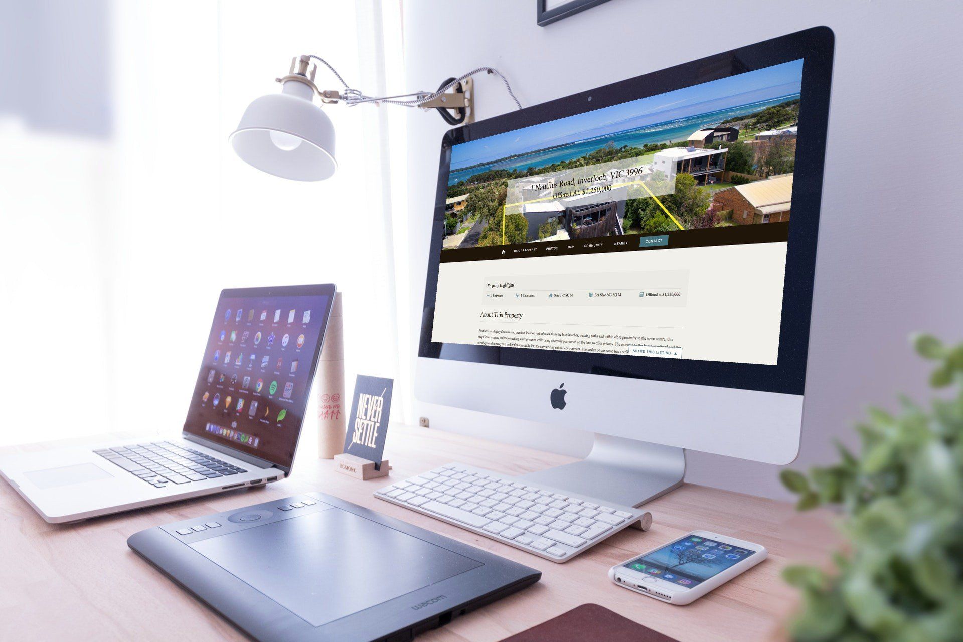 Modern home office desk with iMac, laptop, tablet, phone, keyboard, lamp, and plant