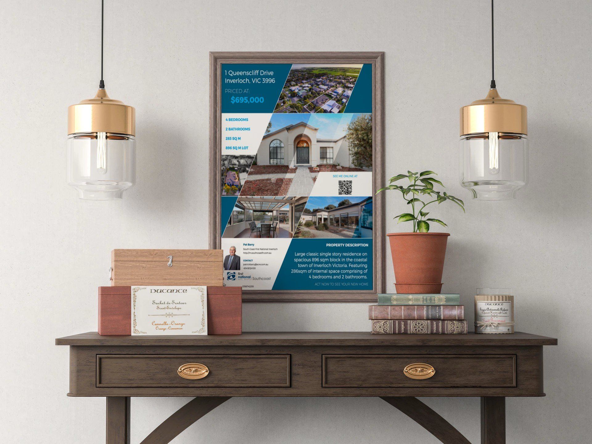 Framed coastal travel poster on a wooden console with books, potted plant, and wall sconces