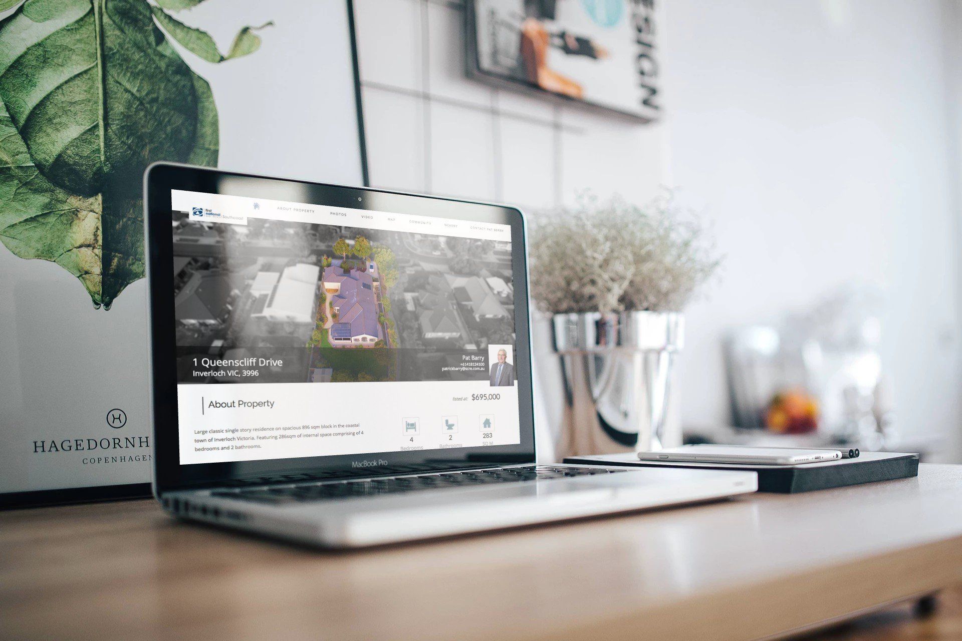 Laptop on a desk displaying a website, with a plant and blurred decor in the background.
