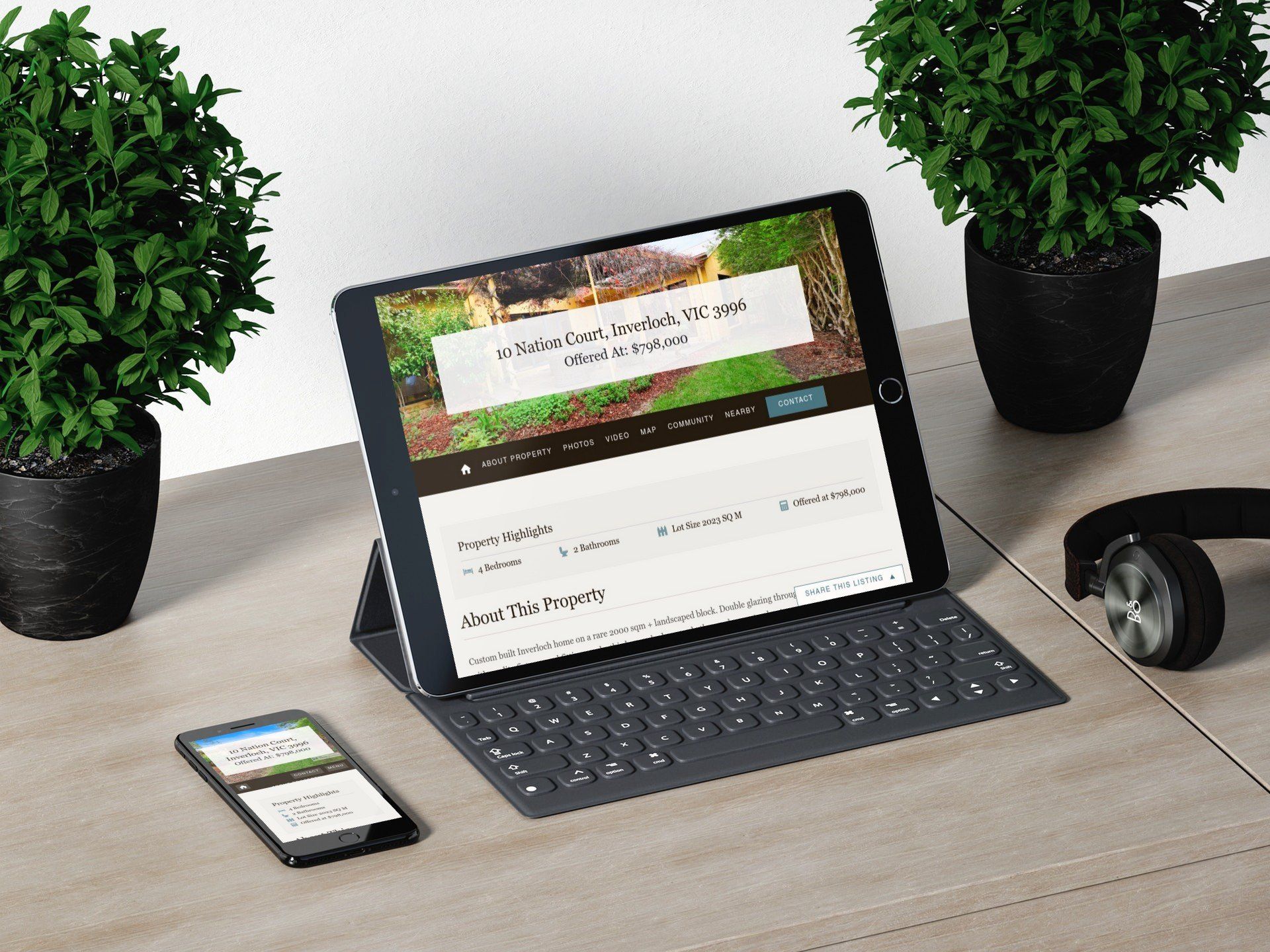 Tablet on a keyboard case beside a smartphone and headphones, with two potted plants on a desk.