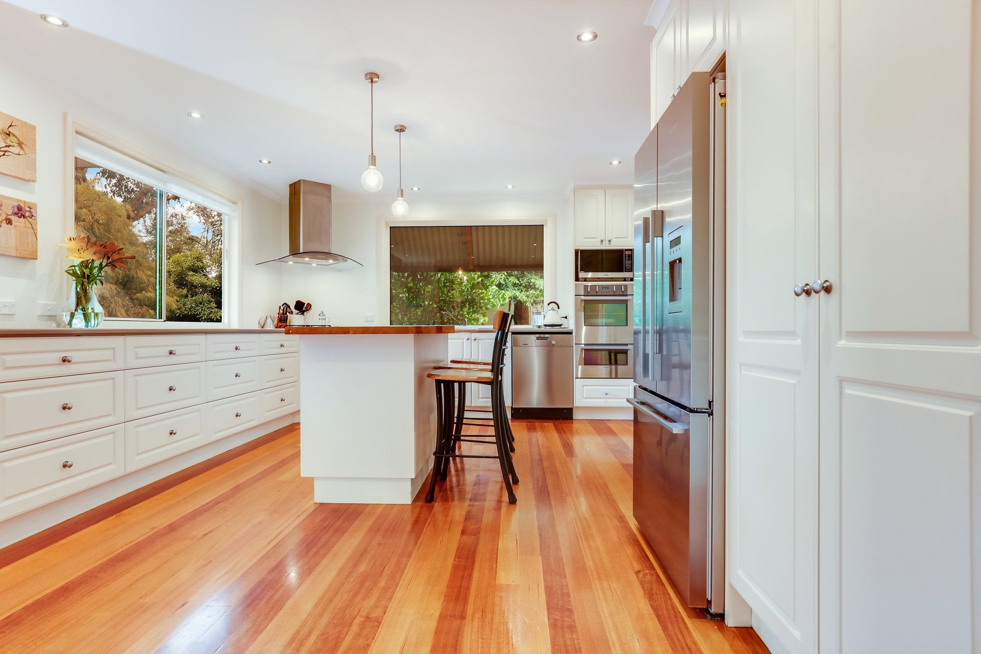 Bright modern kitchen with hardwood floors, white cabinets, island, and stainless steel appliances