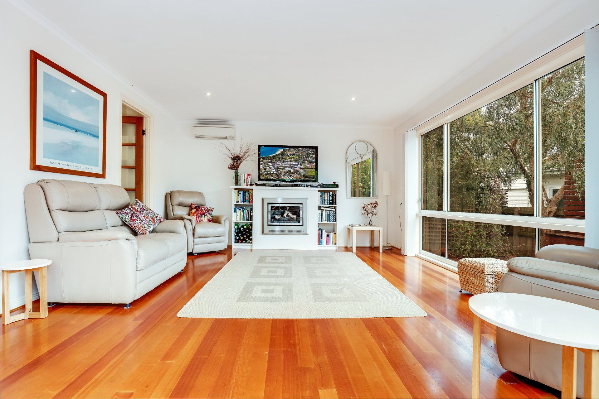 Bright living room with white sofa, hardwood floors, large window, and fireplace mantel