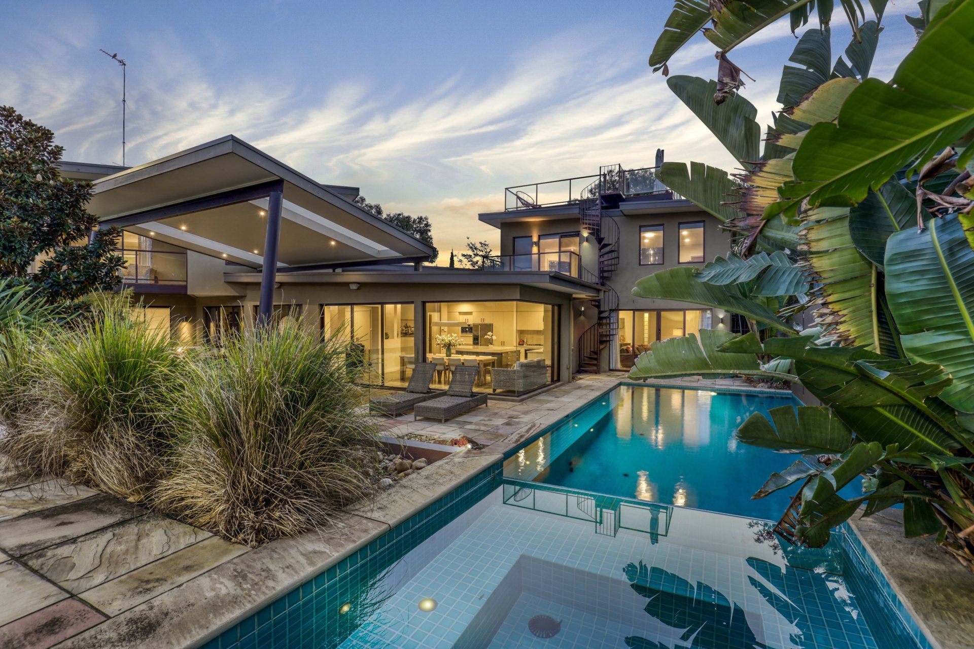 Modern house with lit pool and tropical landscaping at dusk