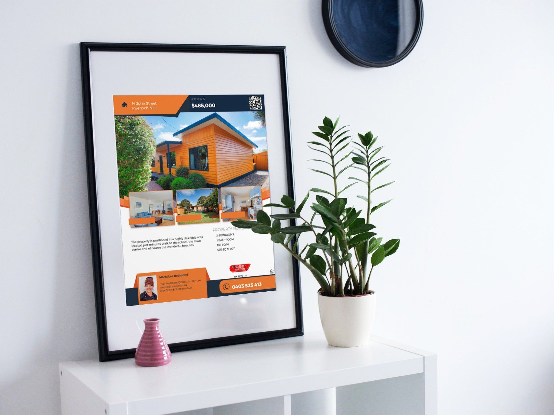 Framed house listing poster on a white shelf beside a potted plant and small decor