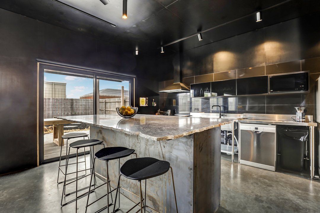 Modern kitchen with black cabinets, marble island, bar stools, and large window overlooking city buildings