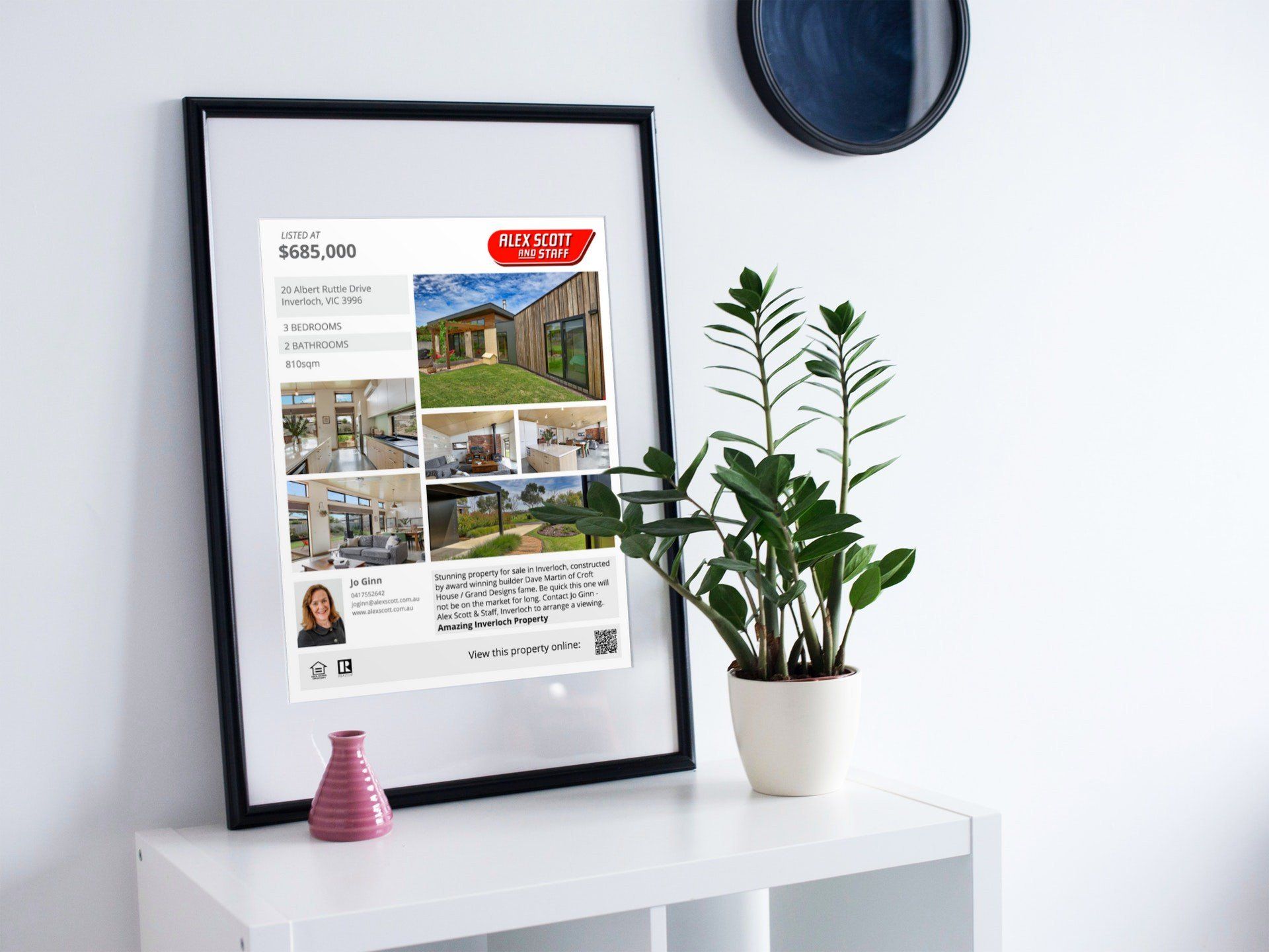 Framed poster on a white shelf beside a potted plant in a bright minimalist room